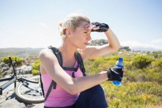photo of woman cyclist holding bottle of energy drink