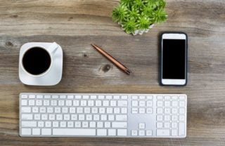 keyboard, smartphone, pen, plant, and coffee on desktop