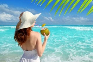 woman on beach drinking from coconut