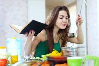 woman cooking with cookbook in hand