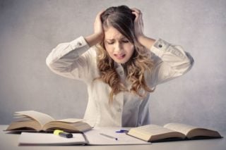 overwhelmed woman sitting at desk covered in books