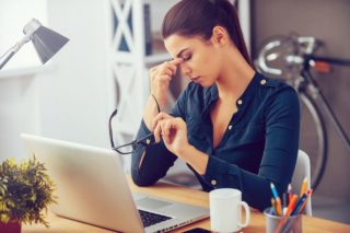 photo depicting woman sitting at work desk, pinching her nose, stressed