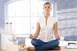 woman meditating on top of an office desk