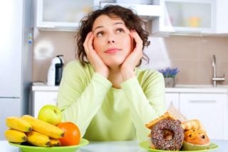 woman trying to decide between healthy fruit and unhealthy donuts and muffins